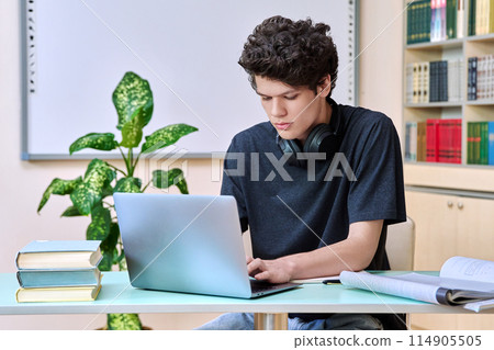Portrait of college student guy sitting at desk with laptop inside an educational library Portrait of college student guy sitting at desk with laptop inside an educational library 114905505