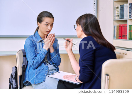 Psychologist behavior talks with upset teenage girl inside educational building 114905509