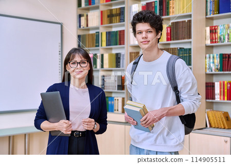 Female teacher with guy college student looking at camera inside library 114905511