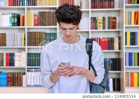 Teenage male student with backpack using smartphone, inside college building, in library 114905514