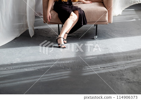 Cropped photo of beautiful female legs in open high-heeled sandals against the background of a concrete floor 114906373