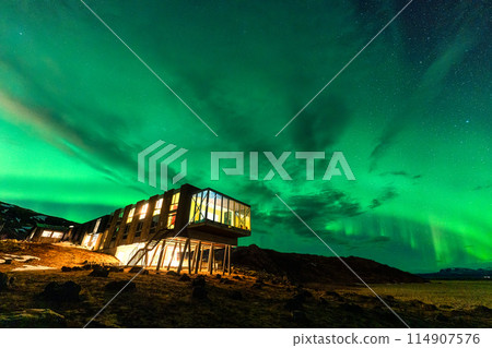 Aurora borealis, Northern lights glowing over luxury hotel on volcanic wilderness in winter at Iceland 114907576