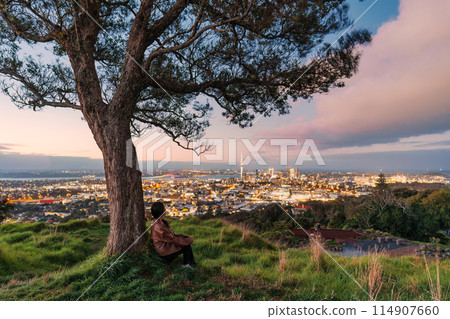 Viewpoint of Mount Eden with female tourist relaxing and sky tower among illuminated city at Auckland, New Zealand 114907660