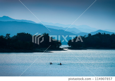 Blue scene of the Kaeng Krachan reservoir with fishing boat and tourist rowing canoe Blue scene of the Kaeng Krachan reservoir with fishing boat and tourist rowing canoe 114907857