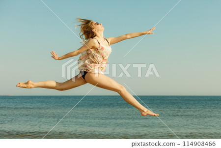 Woman wearing dress playing, jumping near sea 114908466