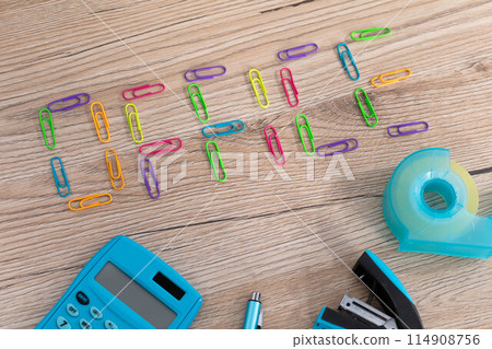 The inscription - office, made of colorful paper clips lying on a wooden desk top. Calculator and other office accessories. 114908756