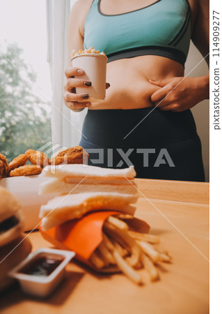To eat or not. Cheerless plump woman looking at the burger while thinking to eat it or not To eat or not. Cheerless plump woman looking at the burger while thinking to eat it or not 114909277