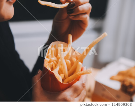 Asian woman holding french fries and eating happily in restaurant Asian woman holding french fries and eating happily in restaurant 114909308