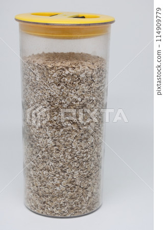 oatmeal in a transparent plastic food jar with a yellow lid on a white background. oatmeal in a transparent plastic food jar with a yellow lid on a white background. 114909779