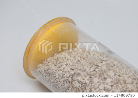 oatmeal in a transparent plastic food jar with a yellow lid on a white background. oatmeal in a transparent plastic food jar with a yellow lid on a white background. 114909780