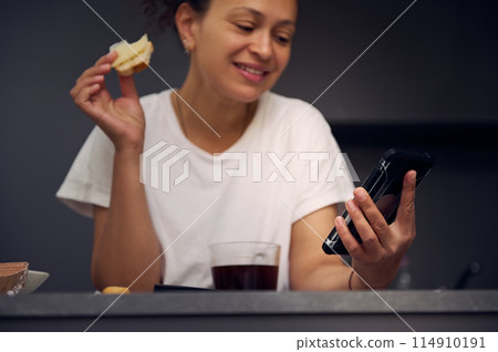 Details on a modern mobile smartphone in hands of a smiling woman, checking social media content, browsing web, scrolling newsfeed, standing at kitchen counter with a sandwich in hand Details on a modern mobile smartphone in hands of a smiling woman, checking social media content, browsing web, scrolling newsfeed, standing at kitchen counter with a sandwich in hand 114910191