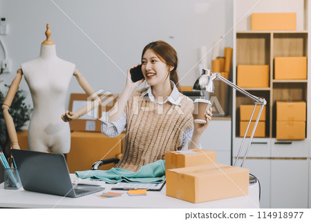 Asian mature female fashion designer works in creative studio, drinking coffee, contemplating and thinking of ideas, imaging dress design collection, and professional boutique tailor SME entrepreneur. Asian mature female fashion designer works in creative studio, drinking coffee, contemplating and thinking of ideas, imaging dress design collection, and professional boutique tailor SME entrepreneur. 114918977