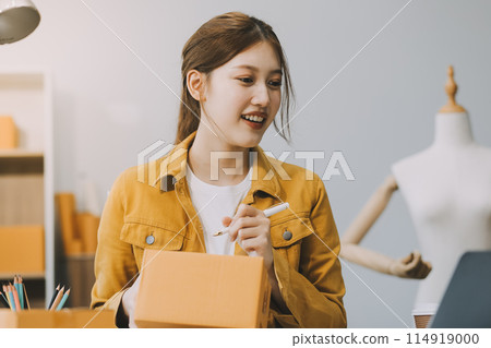 Asian SME business women use laptop computer checking customer order online shipping boxes at home. Starting Small business entrepreneur SME freelance. Online business, Work at home concept. Asian SME business women use laptop computer checking customer order online shipping boxes at home. Starting Small business entrepreneur SME freelance. Online business, Work at home concept. 114919000