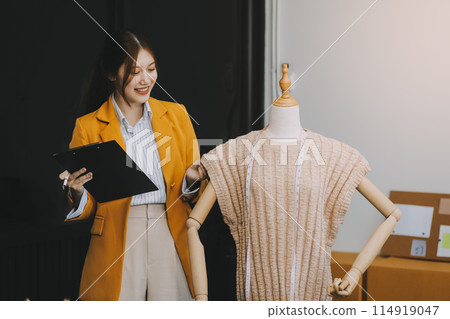 Portrait beautiful smile asian designer woman use computer in tailer fabric fashion small business online workshop. Young owner startup entrepreneur. Creative girl textile garment sme business concept Portrait beautiful smile asian designer woman use computer in tailer fabric fashion small business online workshop. Young owner startup entrepreneur. Creative girl textile garment sme business concept 114919047