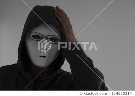 A man wearing a white mask and glasses holding his head 114920314
