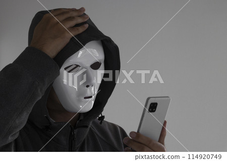A man wearing a white mask and holding a smartphone. He holds his head. 114920749