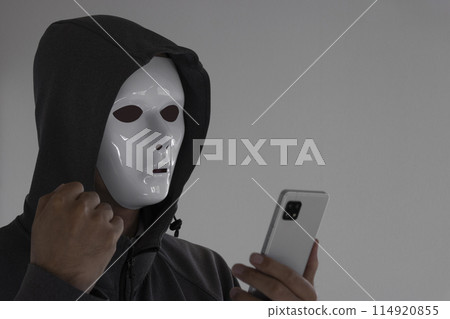 A man wearing a white mask and holding a smartphone. 114920855