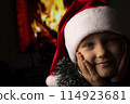 Close-up of girls in Santa's hat on background of fireplace. High quality photo 114923681