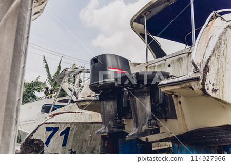 Old and rusty motor boats on a landfill surrounded by tropical forest 114927966