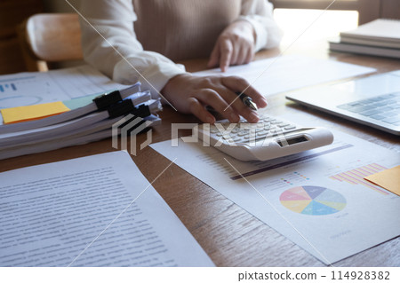 Cropped image of professional businesswoman, entrepreneur or accountant working on a financial report paperwork at her desk, using calculator or laptop. 114928382
