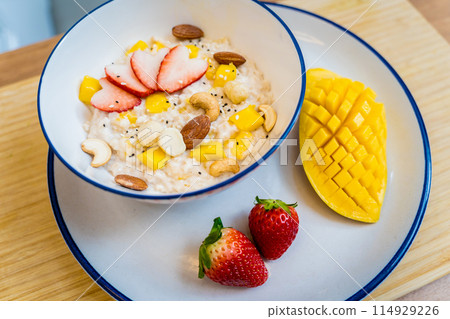 A bowl of oats with strawberries and mango arranged on a plate A bowl of oats with strawberries and mango arranged on a plate 114929226