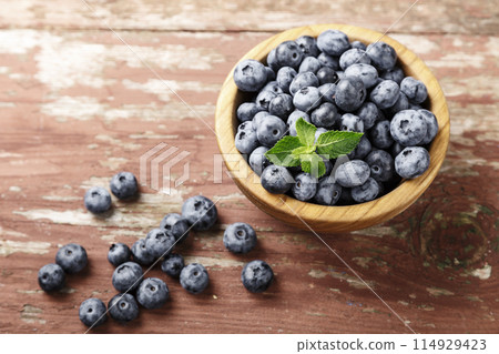 Blueberry berries with mint leaves are in a wooden plate on wooden background. Blueberry berries with mint leaves are in a wooden plate on wooden background. 114929423