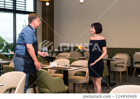 A cafe worker treats a customer to a glass of orange juice A cafe worker treats a customer to a glass of orange juice 114930489