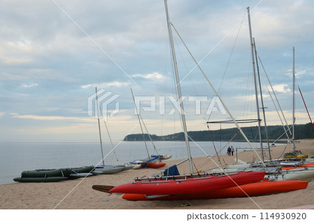 Catamarans with masts on lake shore. 114930920
