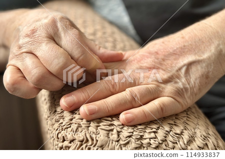 An unfamiliar elderly woman sitting in an armchair makes herself a hand massage with a massager, presses on specific places on the bones of the arm and skin. Health maintenance and Promotion Program An unfamiliar elderly woman sitting in an armchair makes herself a hand massage with a massager, presses on specific places on the bones of the arm and skin. Health maintenance and Promotion Program 114933837