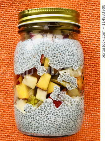 A lot of healthy Chia pudding with coconut milk in a glass containers can with fresh pieces of apple, pear, peach in the refrigerator on the shelf. Close-up A lot of healthy Chia pudding with coconut milk in a glass containers can with fresh pieces of apple, pear, peach in the refrigerator on the shelf. Close-up 114933909