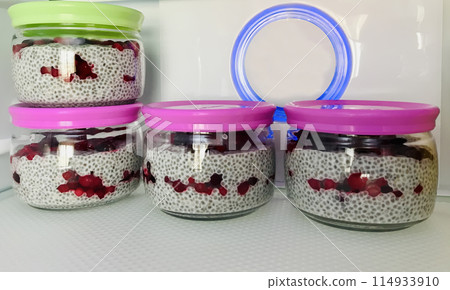 A lot of healthy Chia pudding with coconut milk in a glass containers can with fresh berries as cranberries, cranberry in the refrigerator on the shelf. Close-up A lot of healthy Chia pudding with coconut milk in a glass containers can with fresh berries as cranberries, cranberry in the refrigerator on the shelf. Close-up 114933910