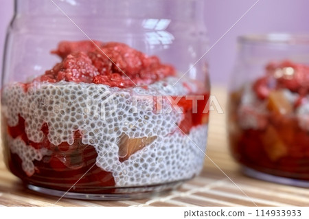 A lot of healthy Chia pudding with coconut milk in a glass containers in view can with fresh berries as raspberry, red currant, cranberry and pieces of peach on bamboo background. Close-up A lot of healthy Chia pudding with coconut milk in a glass containers in view can with fresh berries as raspberry, red currant, cranberry and pieces of peach on bamboo background. Close-up 114933933