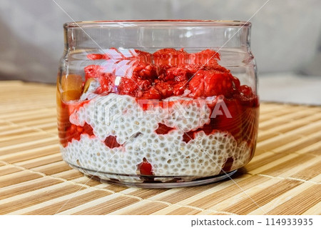 Healthy Chia pudding with coconut milk in glass container in view can with fresh berries as raspberry, red currant, cranberry and pieces of peach on bamboo background on store counter. Close-up Healthy Chia pudding with coconut milk in glass container in view can with fresh berries as raspberry, red currant, cranberry and pieces of peach on bamboo background on store counter. Close-up 114933935
