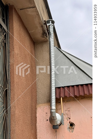 A metal pipe is attached to the wall of a brick building, which removes smoke from the room. This is a device for air circulation 114933959