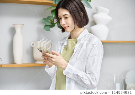 一位年輕女子在房間裡看著她的智慧型手機 一位年輕女子在房間裡看著她的智慧型手機 114934981