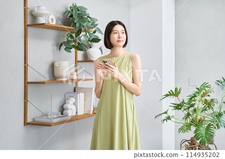 一位穿著夏裝的年輕女子在房間裡操作智慧型手機 一位穿著夏裝的年輕女子在房間裡操作智慧型手機 114935202