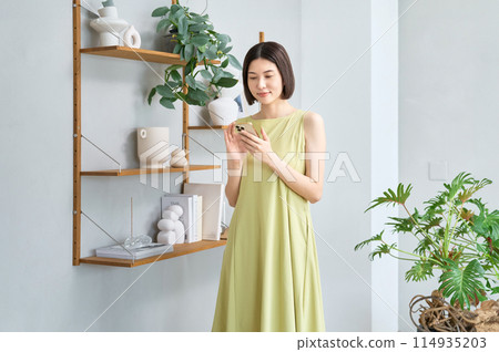 A young woman in summer clothes operating a smartphone in a room A young woman in summer clothes operating a smartphone in a room 114935203