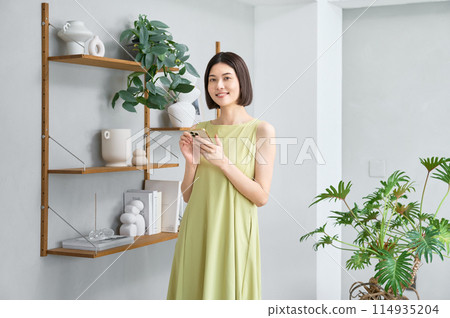 一位穿著夏裝的年輕女子在房間裡操作智慧型手機 114935204