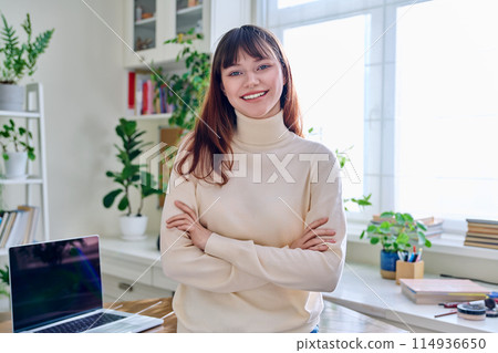 Portrait of smiling female student, 19,20 years old, looking at camera, in home interior Portrait of smiling female student, 19,20 years old, looking at camera, in home interior 114936650