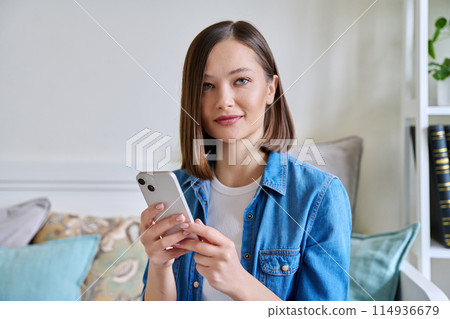 Young woman using smartphone sitting on couch at home 114936679