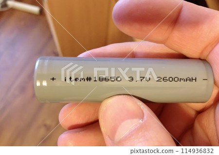 Unknown person hand holding a new 18650 type rechargeable battery. Using high capacity li-ion battery in electronics and devices. Close-up Unknown person hand holding a new 18650 type rechargeable battery. Using high capacity li-ion battery in electronics and devices. Close-up 114936832