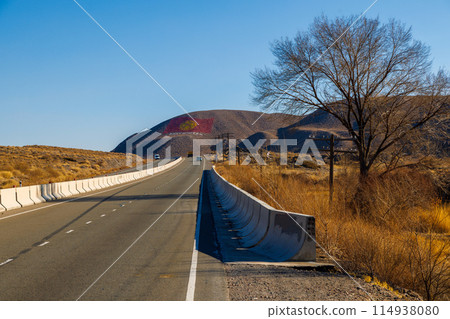 A road with concrete barrier winding through natural landscape. The flag of Kyrgyzstan is drawn on a mountain at sunny autumn day. 114938080