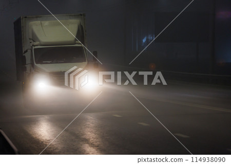 A truck with headlights driving on a foggy highway at midnight A truck with headlights driving on a foggy highway at midnight 114938090