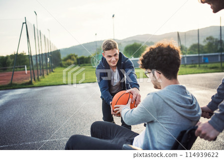 Disabled young man in a wheelchair playing basketball with his friends. Teamwrok and male friendship. Disabled young man in a wheelchair playing basketball with his friends. Teamwrok and male friendship. 114939622