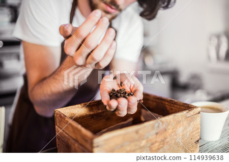 Handsome barista working in coffee shop, smelling coffee beans. University student working part-time in cafe. Handsome barista working in coffee shop, smelling coffee beans. University student working part-time in cafe. 114939638