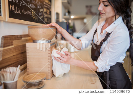 Shop assistant serving customer in package-free store using reusable containers. Zero waste shops offering package-free bulk goods and sustainable alternatives. 114939670