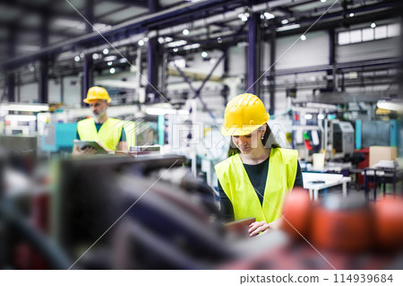 Warehouse employees in warehouse. Two workers in reflective clothing in modern industrial factory, heavy industry, manufactrury. 114939684