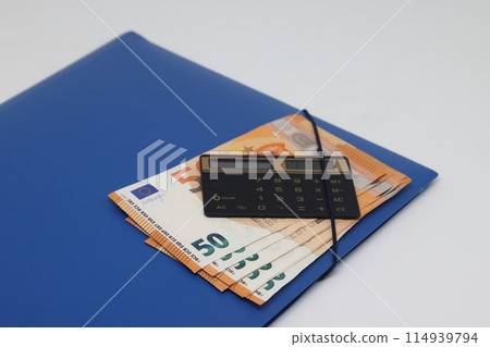 Calculator and banknotes lie on a folder for papers, financial accounting and control. Calculator and banknotes lie on a folder for papers, financial accounting and control. 114939794