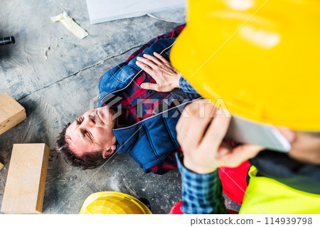 Colleague giving first aid to unconscious worker after accident, calling ambulance. Concept of occupational safety and health in workplace. 114939798