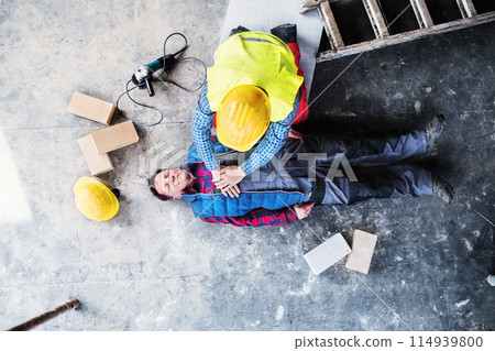 Colleague performing CPR on an injured worker lying on the ground after accident. Concept of occupational safety and health in workplace. 114939800